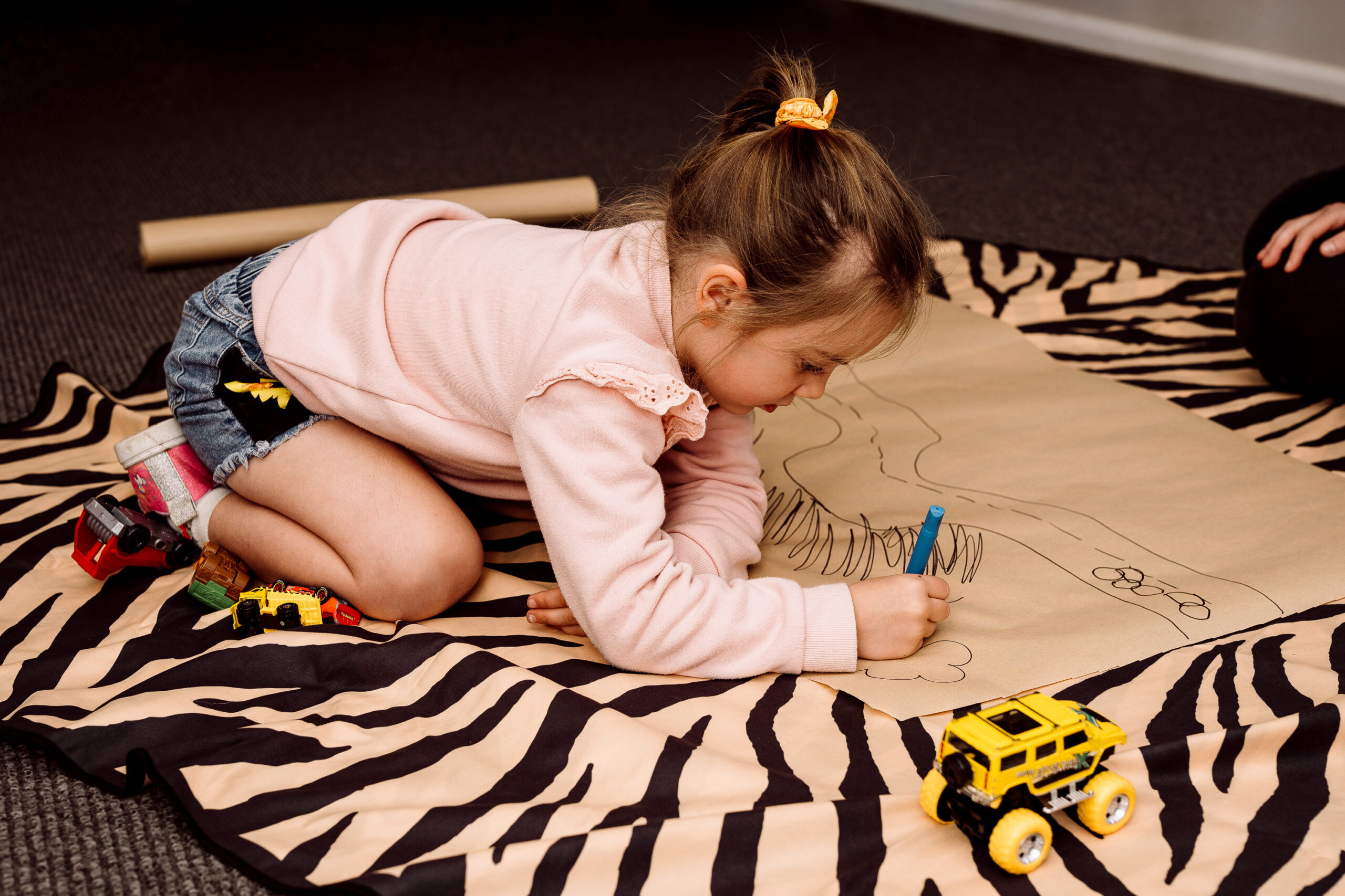 A young girl draws on paper on the floor.